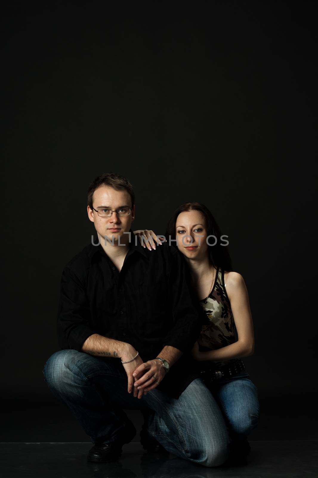 handsome young couple posing sitting in studio on black background