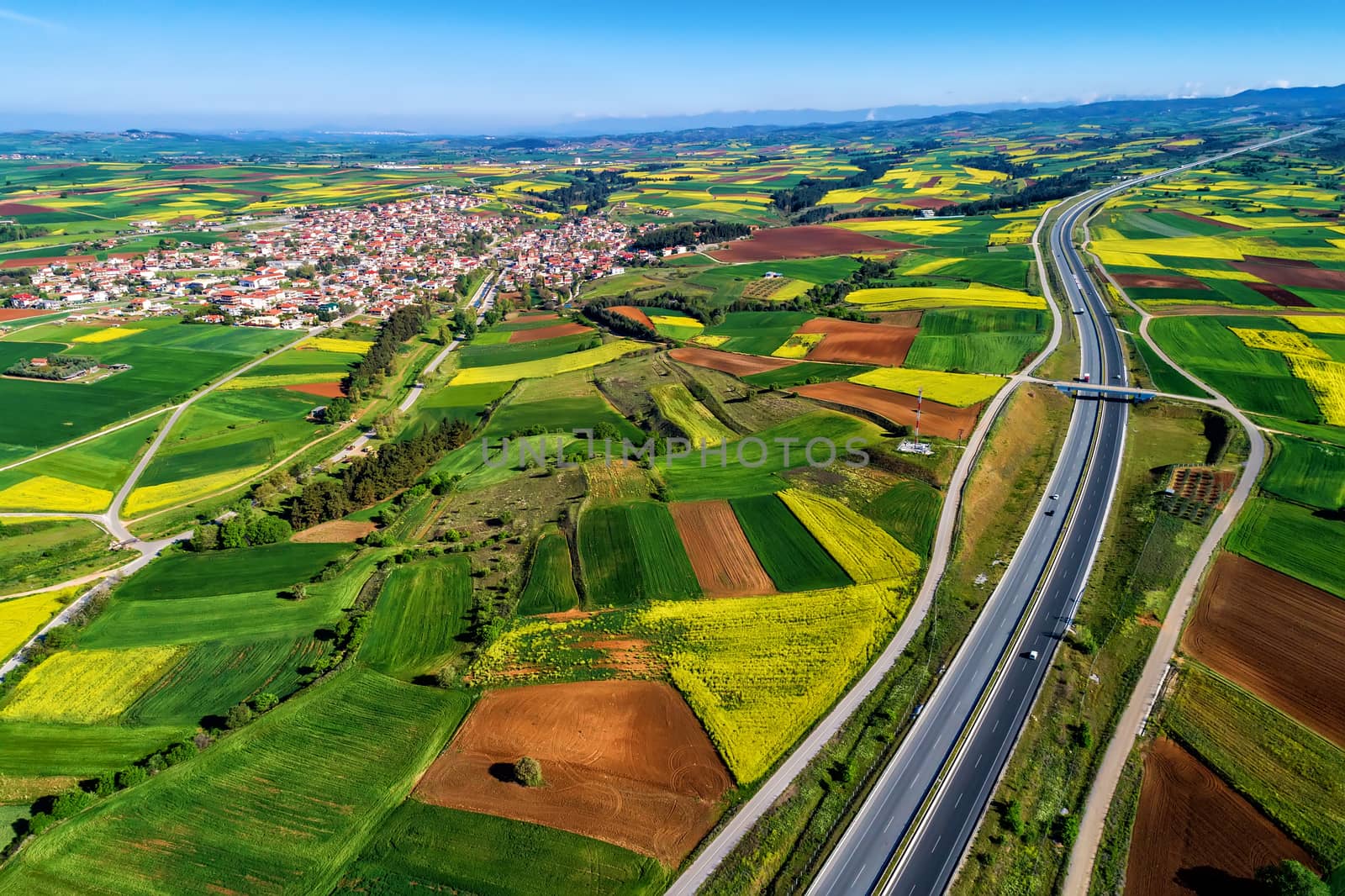 Aerial view of road passing through a rural landscape with blooming rape in northern Greece