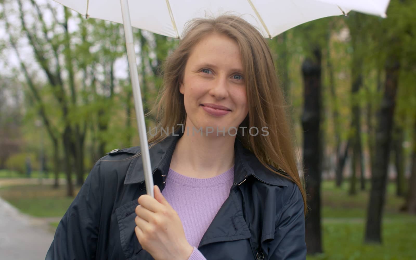 Beautiful smiling woman with umbrella under rain in the park. Outdoors portrait of young blond woman. Real people.