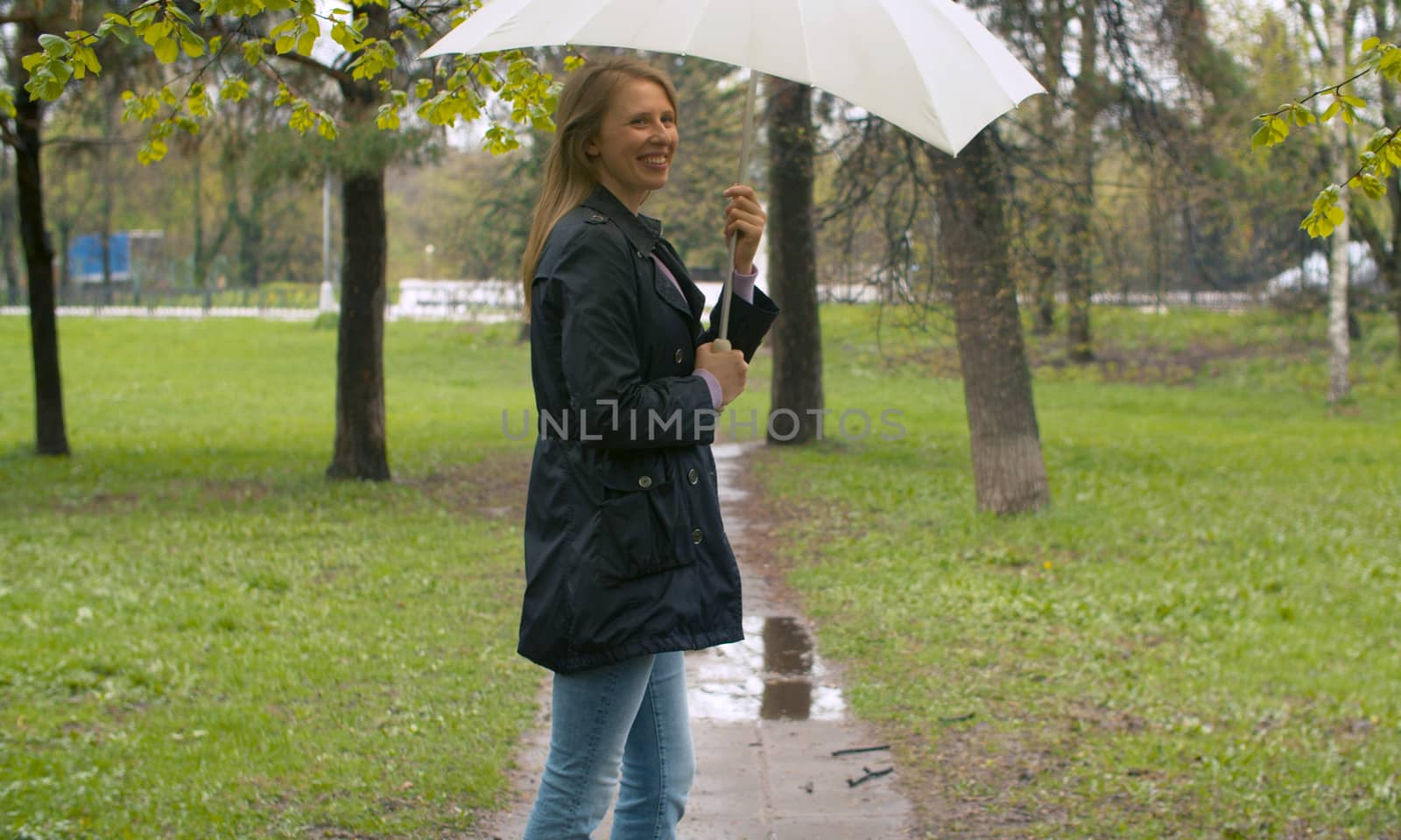 Rainy day in the park. Attractive smiling woman with umbrella under rain. Outdoors female portrait. Real people