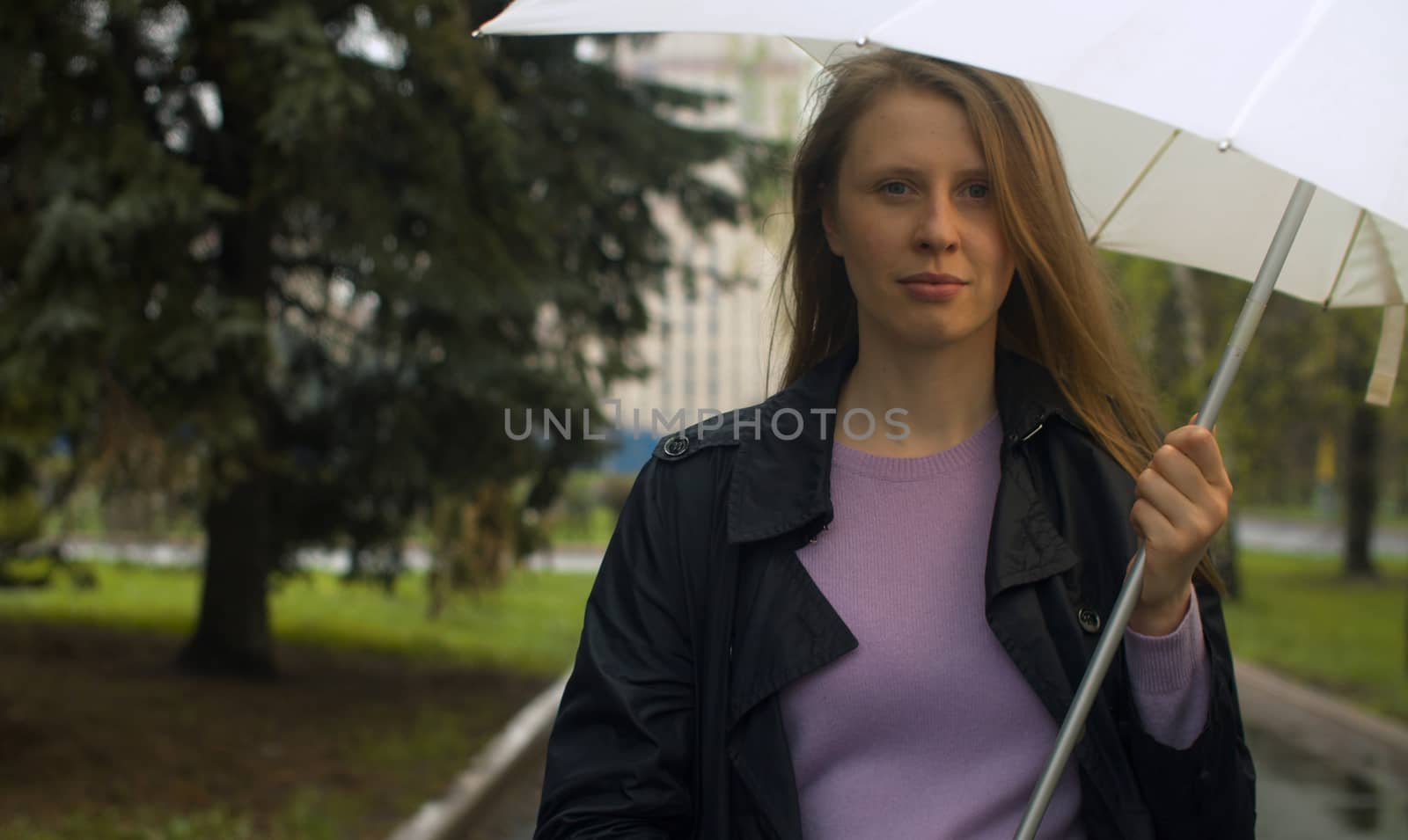 Portrait of a serious young woman with umbrella under rain in the park.
