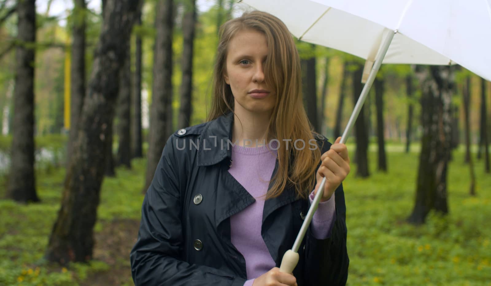 Rainy day in the park. Attractive woman walking with umbrella under rain. Outdoors female portrait. Real people