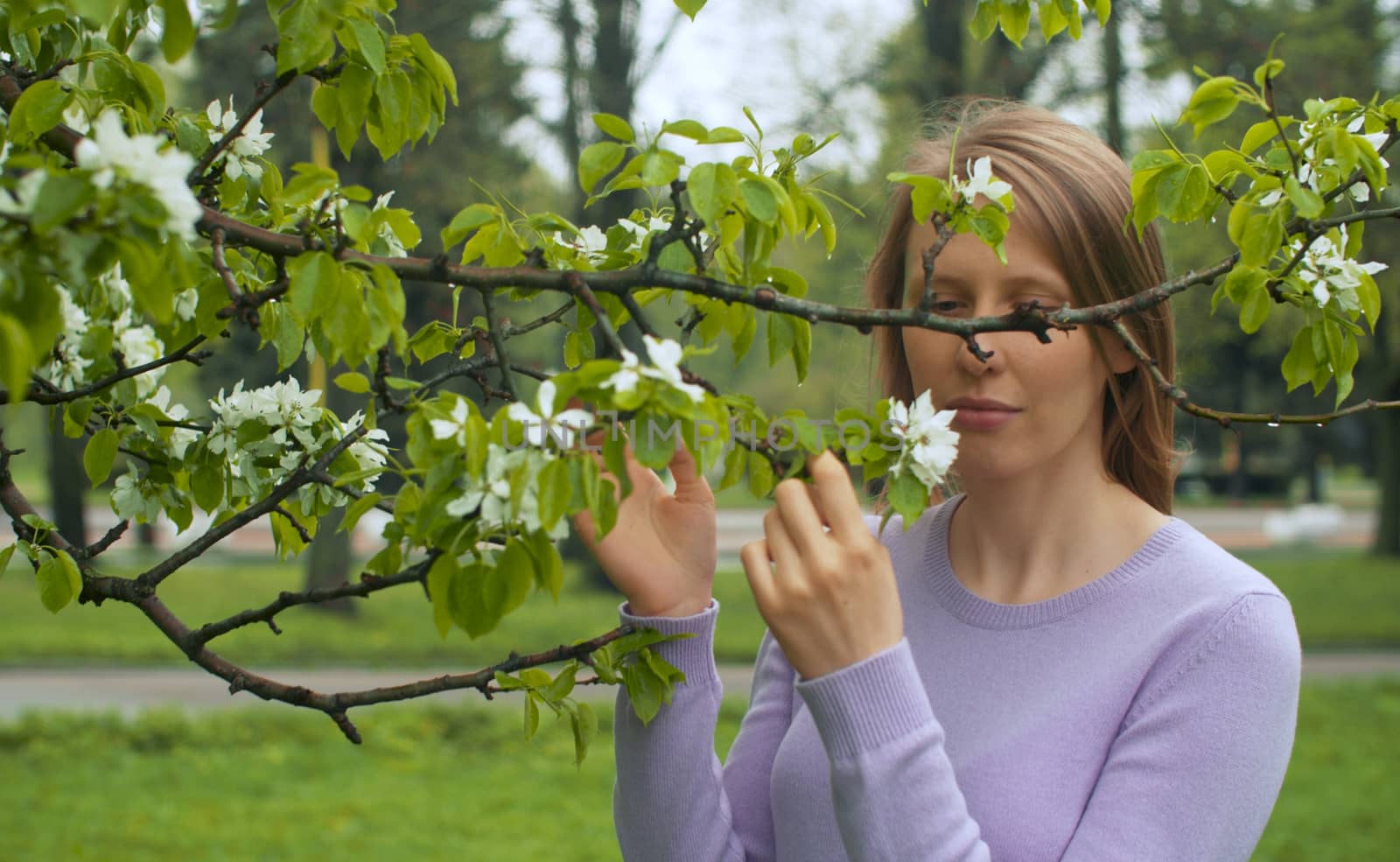 Close up portrait of happy woman near apple tree in blossom. She is watching flowers. Beauty in nature. Real people