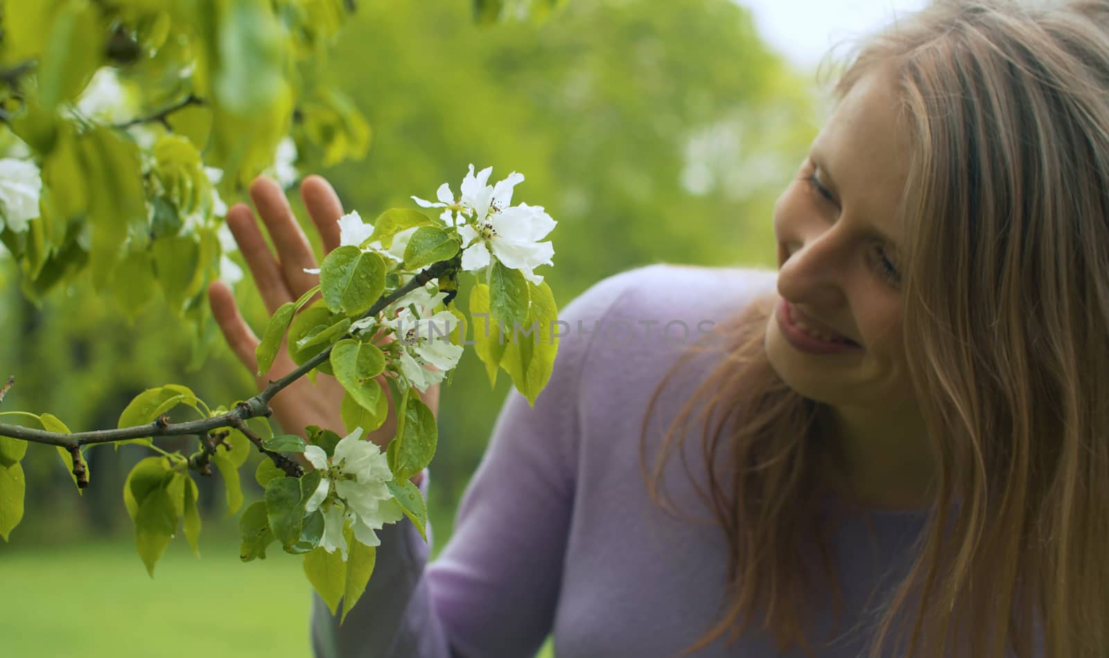 Close up portrait of happy woman near apple tree in blossom. She is watching flowers. Beauty in nature. Real people