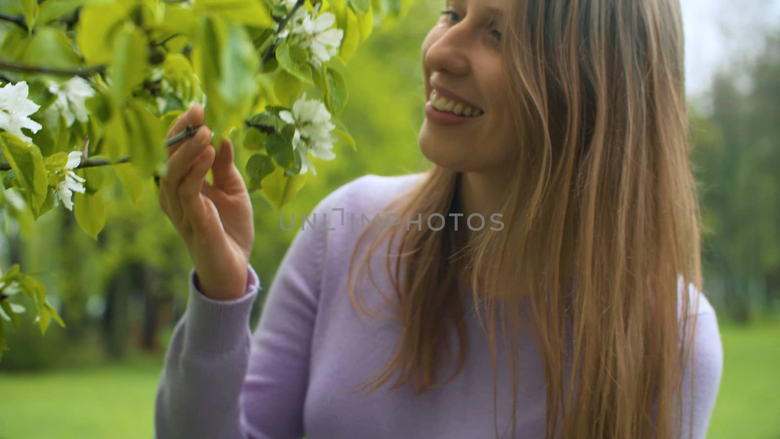 Close up portrait of happy woman near apple tree in blossom. She is watching flowers. Beauty in nature. Real people