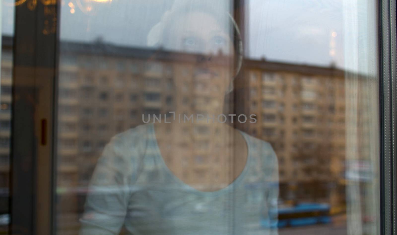 Portrait of a young beautiful woman washing a window, view through a glass outside. Buildings reflected in the window. Domestic daily life, housekeeping