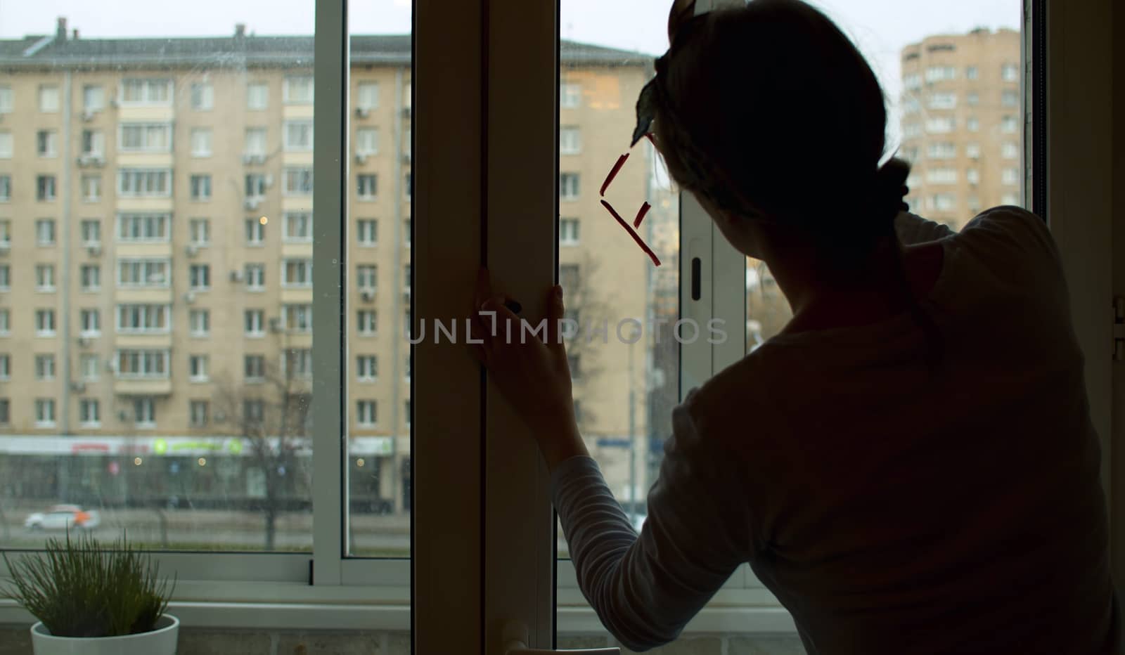 Silhouette of a young woman writing on window glass using lipstick. Rear view