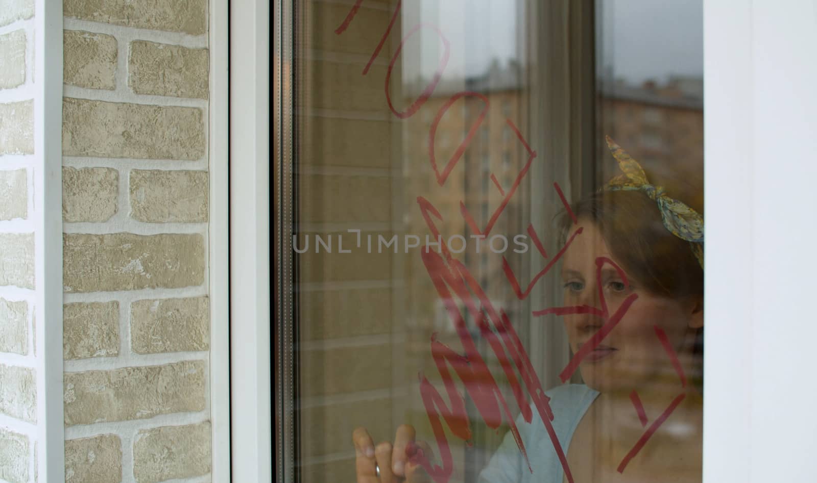 Young beautiful woman writing word "Freedom" on the window glass using lipstick. The end of quarantine. View through a glass outside. Buildings reflected in the window.