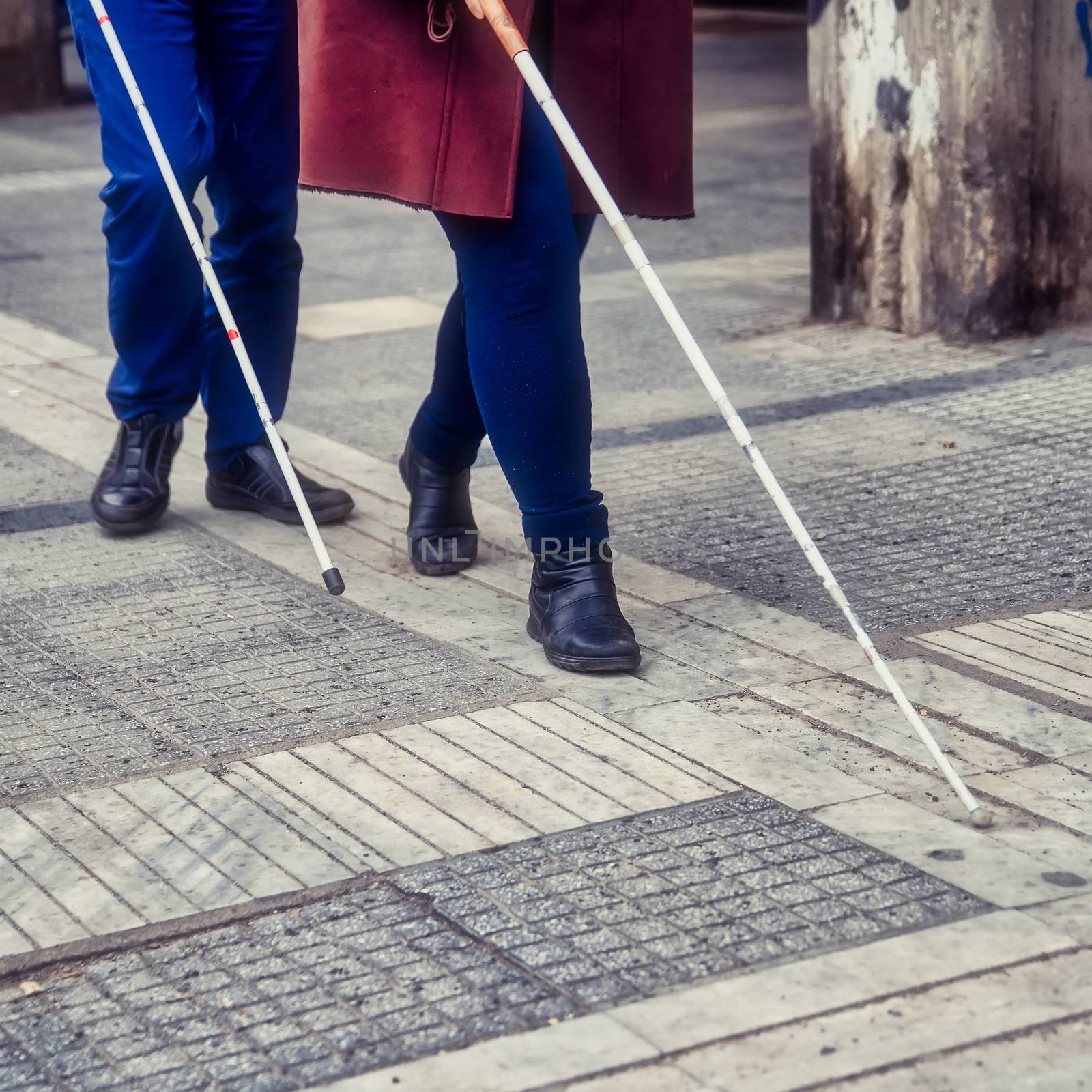 blind man and woman walking on the street using a white walking  by ververidis