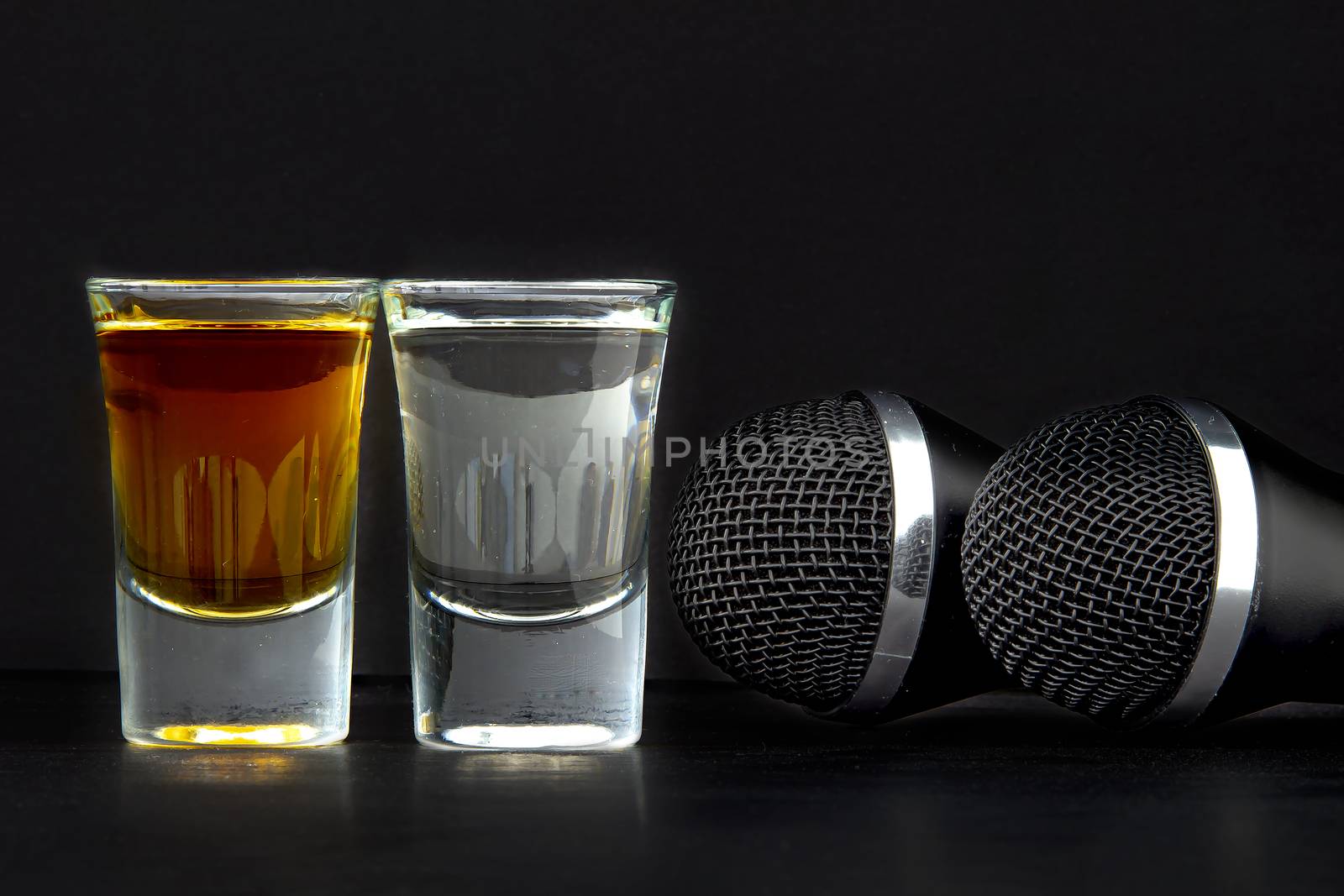Shoot Glasses with liquor and two karaoke microphones on a black background by oasisamuel