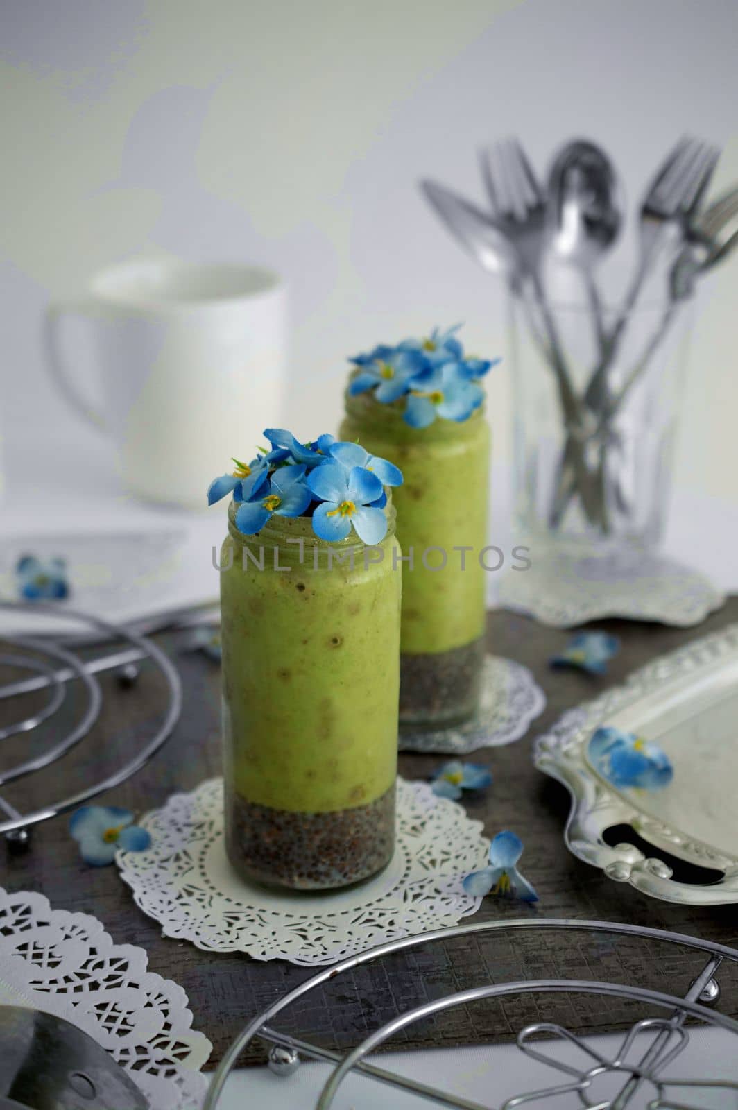Healthy green milkshake with blue flowers in a decorated table with white pattern cloths underneath