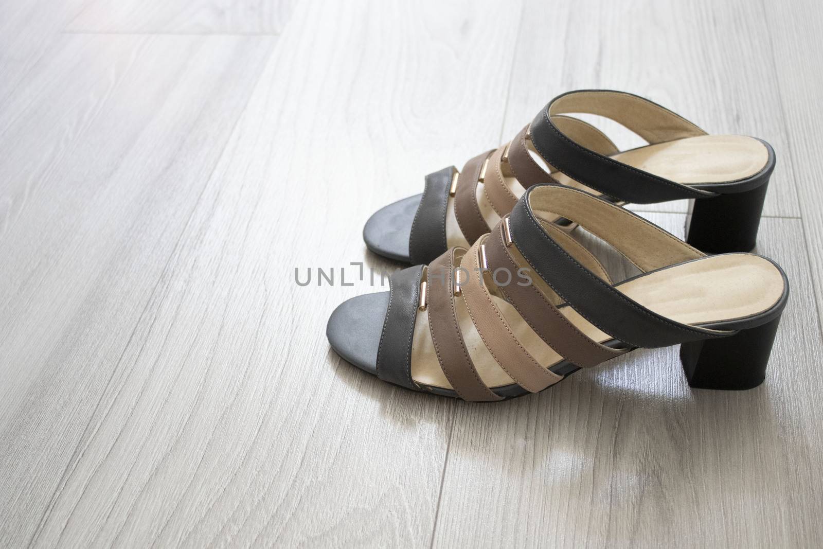 Women's shoes with small heels with straps stand on a gray parquet. The straps are fastened with metal parts