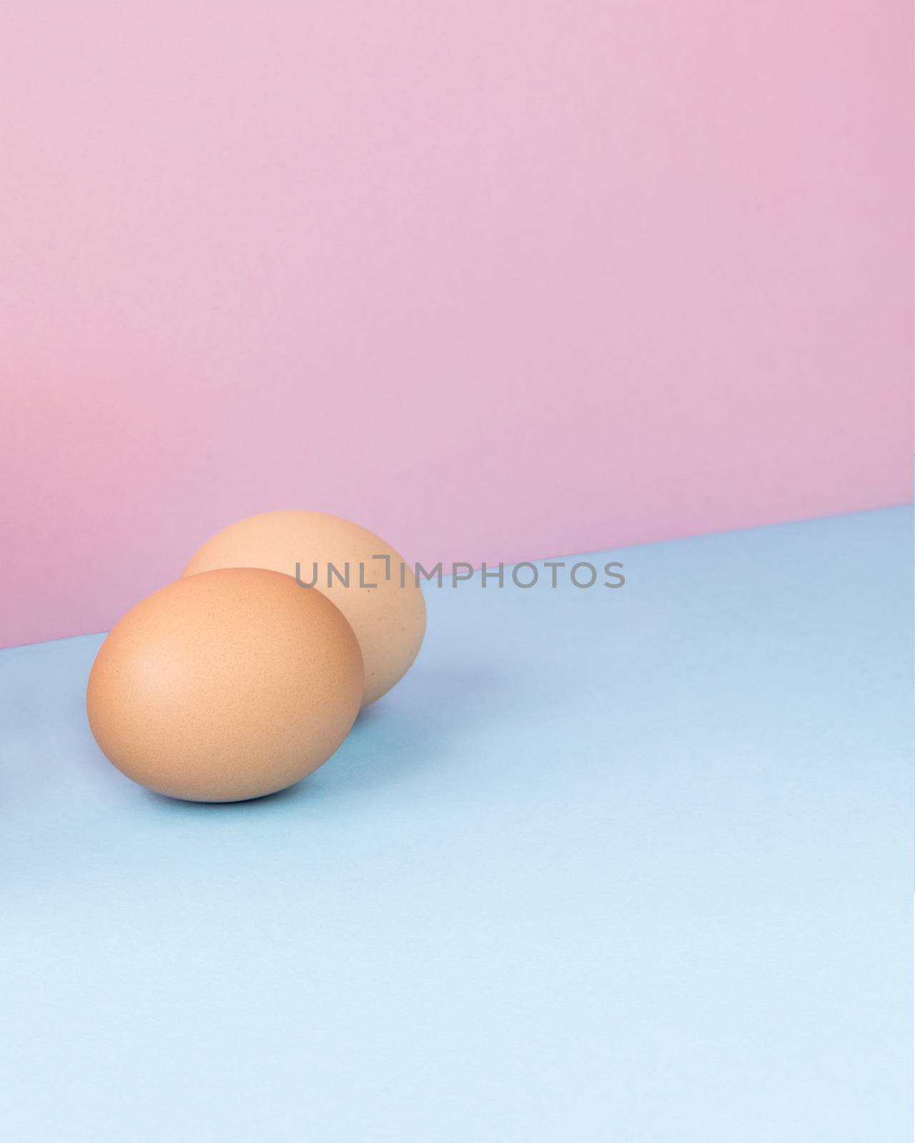 Minimalist image of two brown eggs on a light blue and pink background. Copy space available.