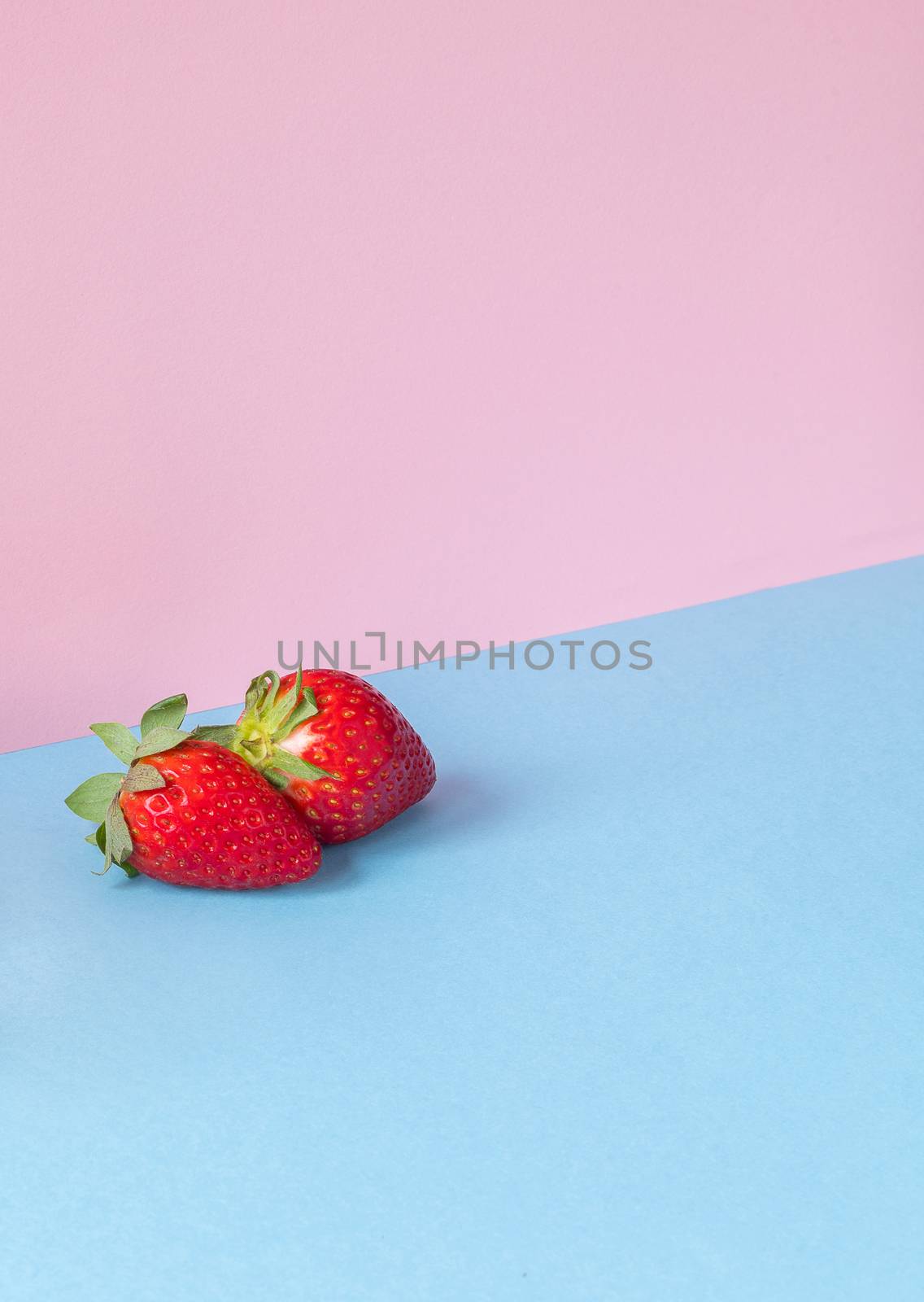 Minimalist image of a couple of strawberries on a light blue and pink background. Copy space available.