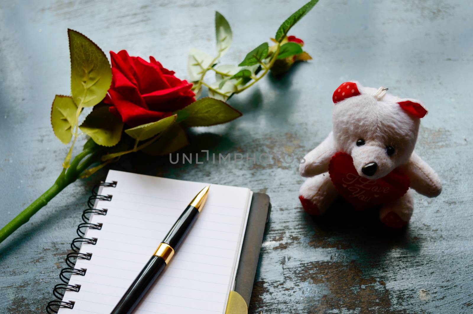 Blank Page Notebook, pen, a beautiful red rose on rustic metal floor background placed near a teddy. Love letter Writing Proposal or propose and waiting concept for valentines day holidays Top view.