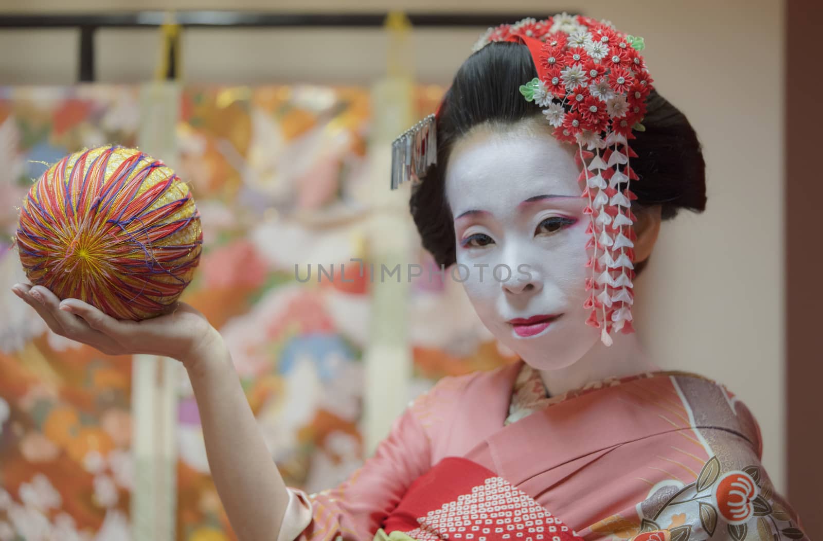 Maiko in kimono holding a temari ball in the hand.