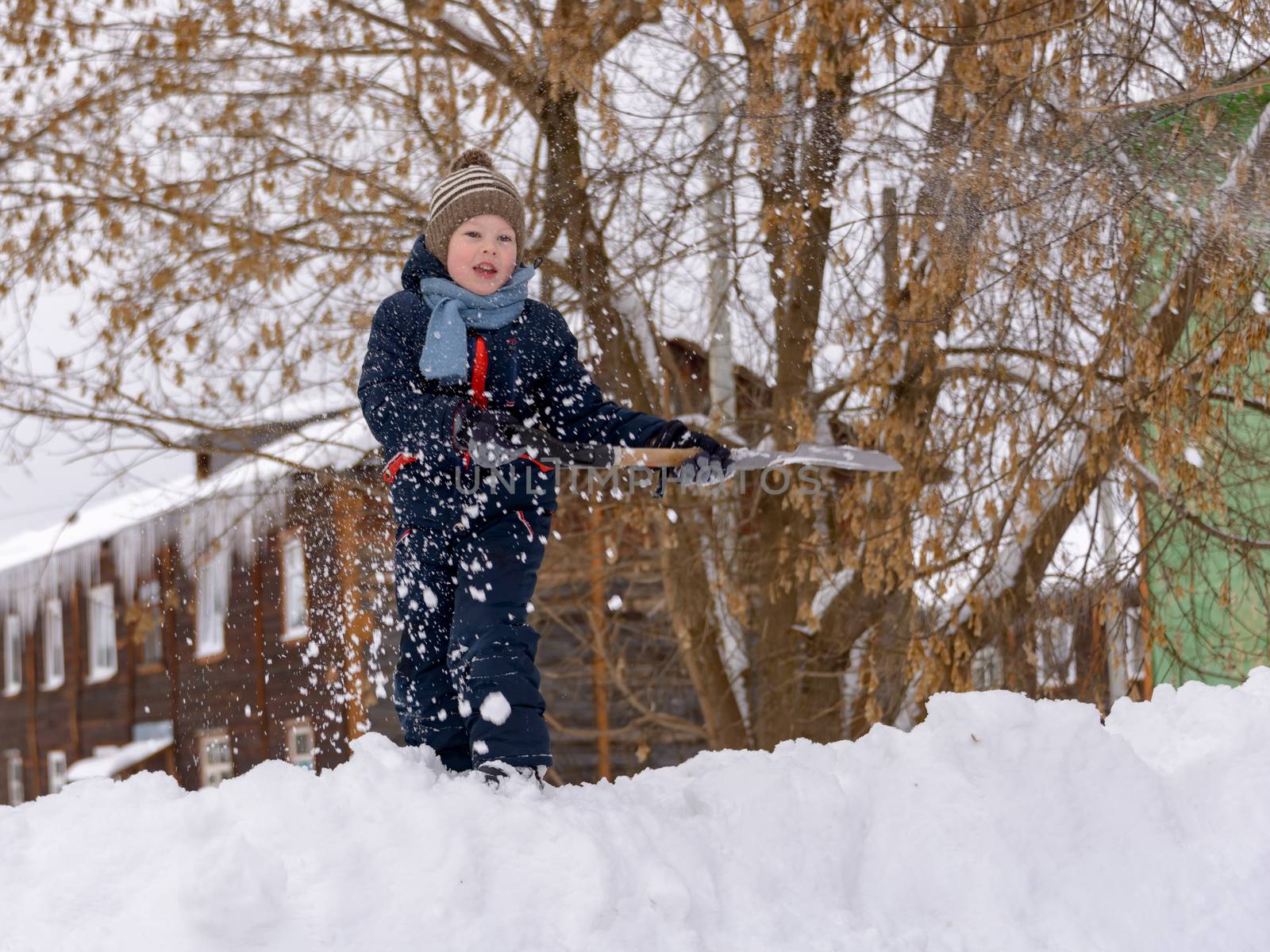 A boy in a knitted hat and with a scarf in winter plays in the snow. by vladali