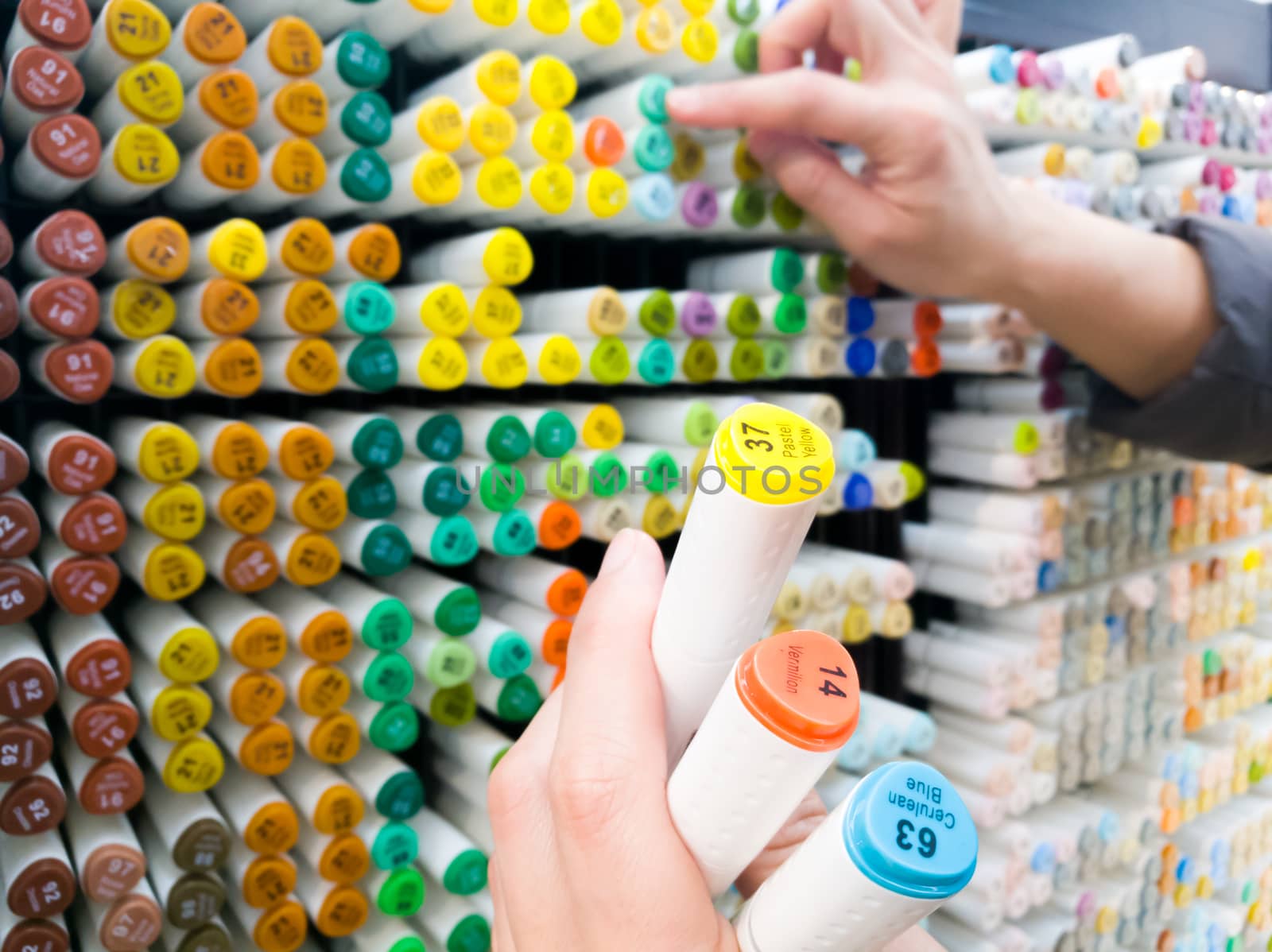 focus on women hand hold the selected color pen with other hand is selecting the color pen on the shelf at stationery shop