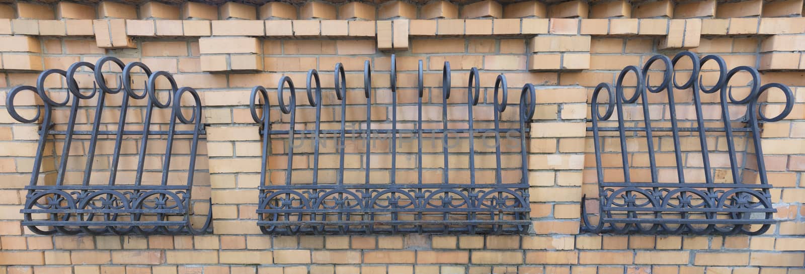 The fence of brickwork is decorated with a forged curly iron grating