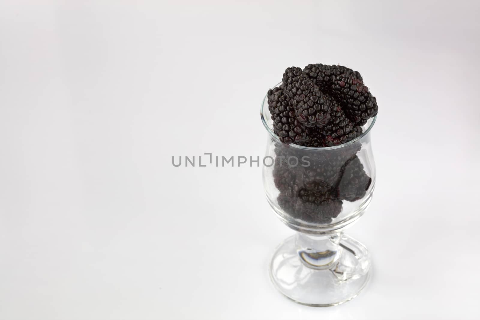 Ripe blackberry are arranged in a clear glass on a light background, a picture in a high key