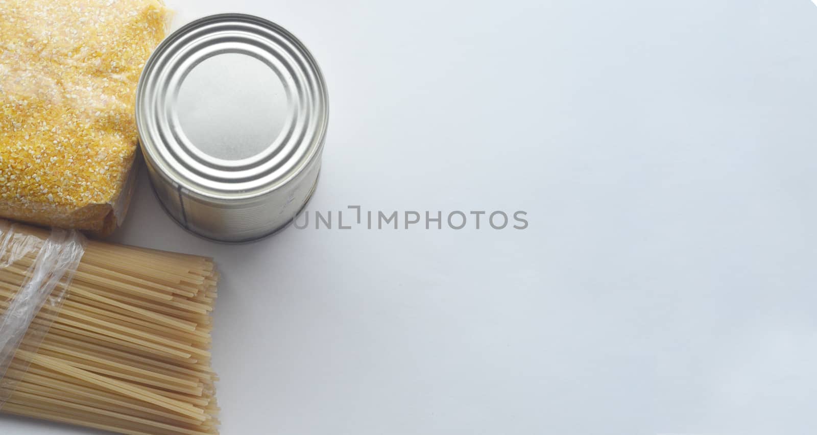 Food supplies, crisis food stock for quarantine isolation period on white background. Pasta, corn grits and canned food. Food delivery, coronavirus quarantine. Copyspace.
