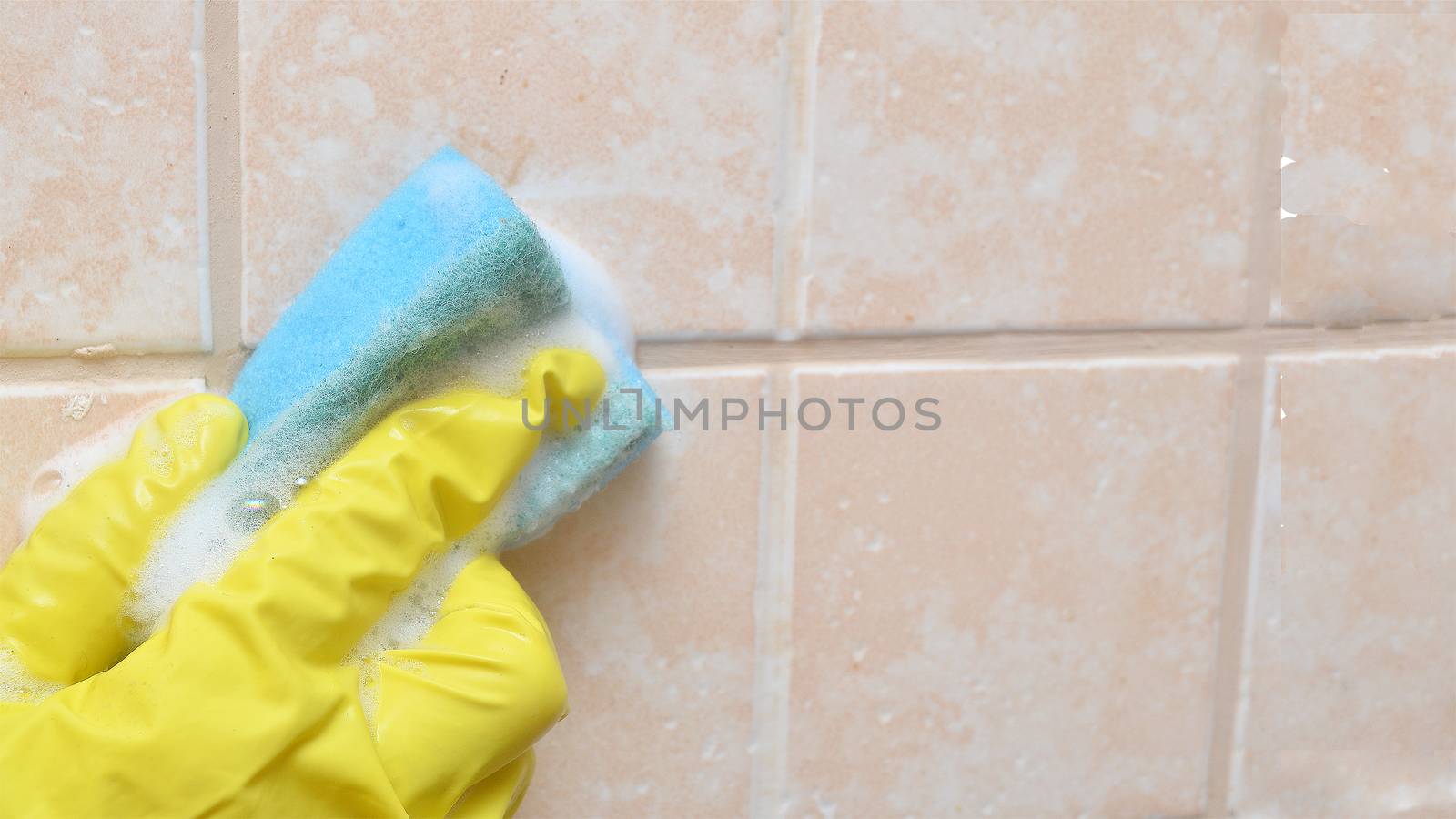 A man in a yellow protective glove washes a dirty ceramic tiles in the bathroom.Homework banner.Copyspace