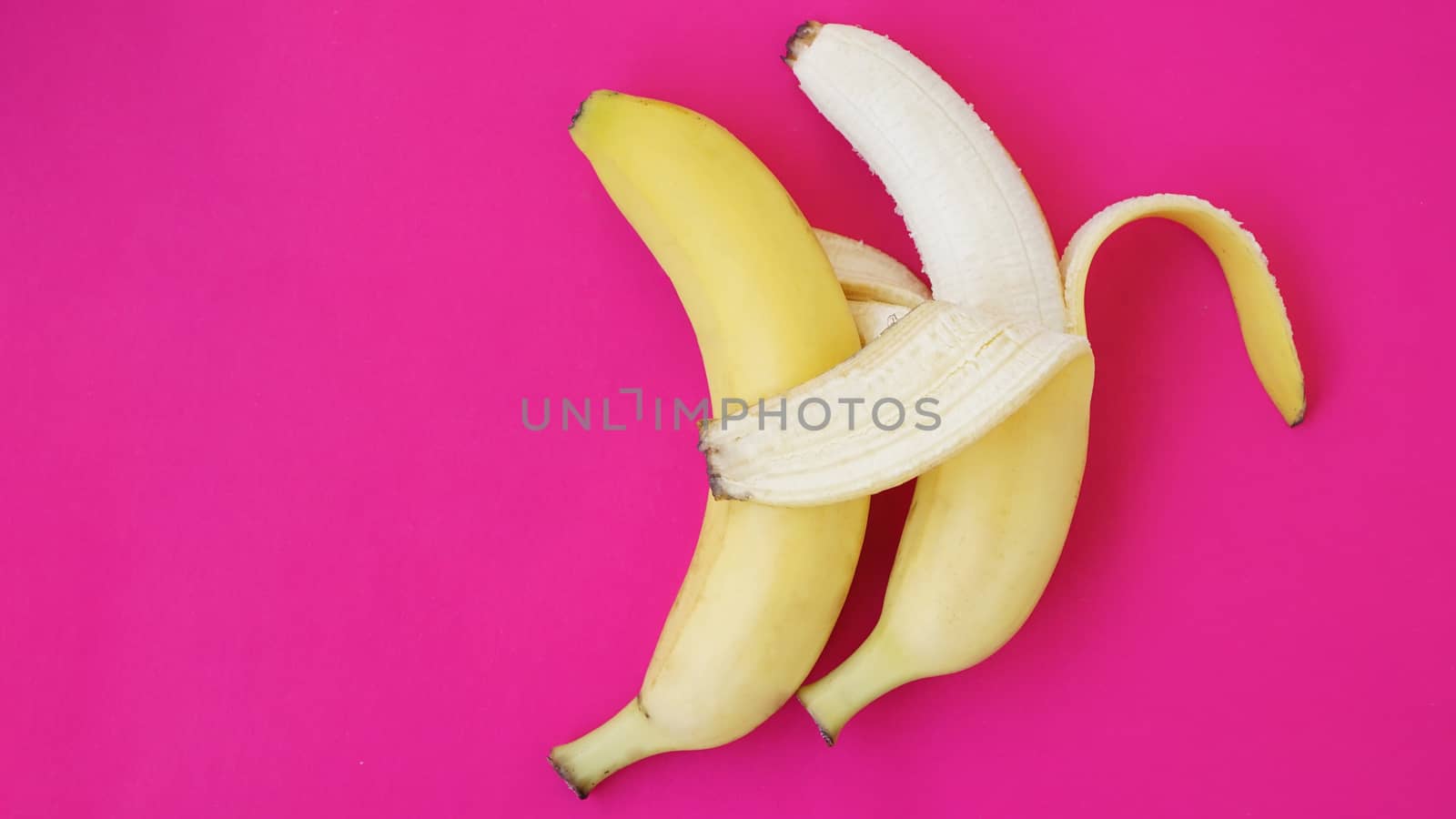 The concept of a friendly couple. Banana like a husband embraces another one like a wife. Gay couple idea. Solid pink background.