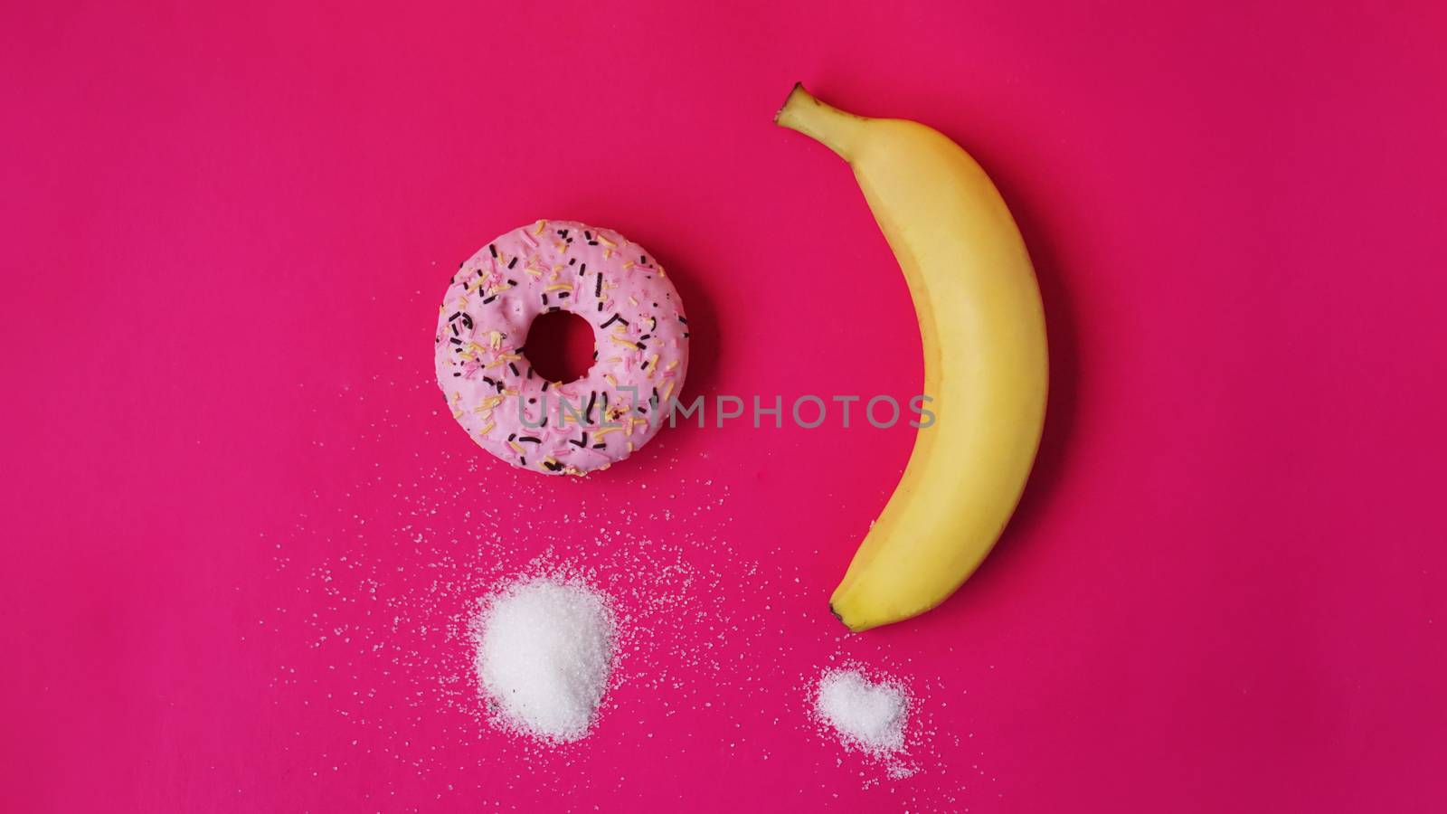 Choice donut against banana - sugar and calories in foods. Starting healthy eating or junk food. Pink background