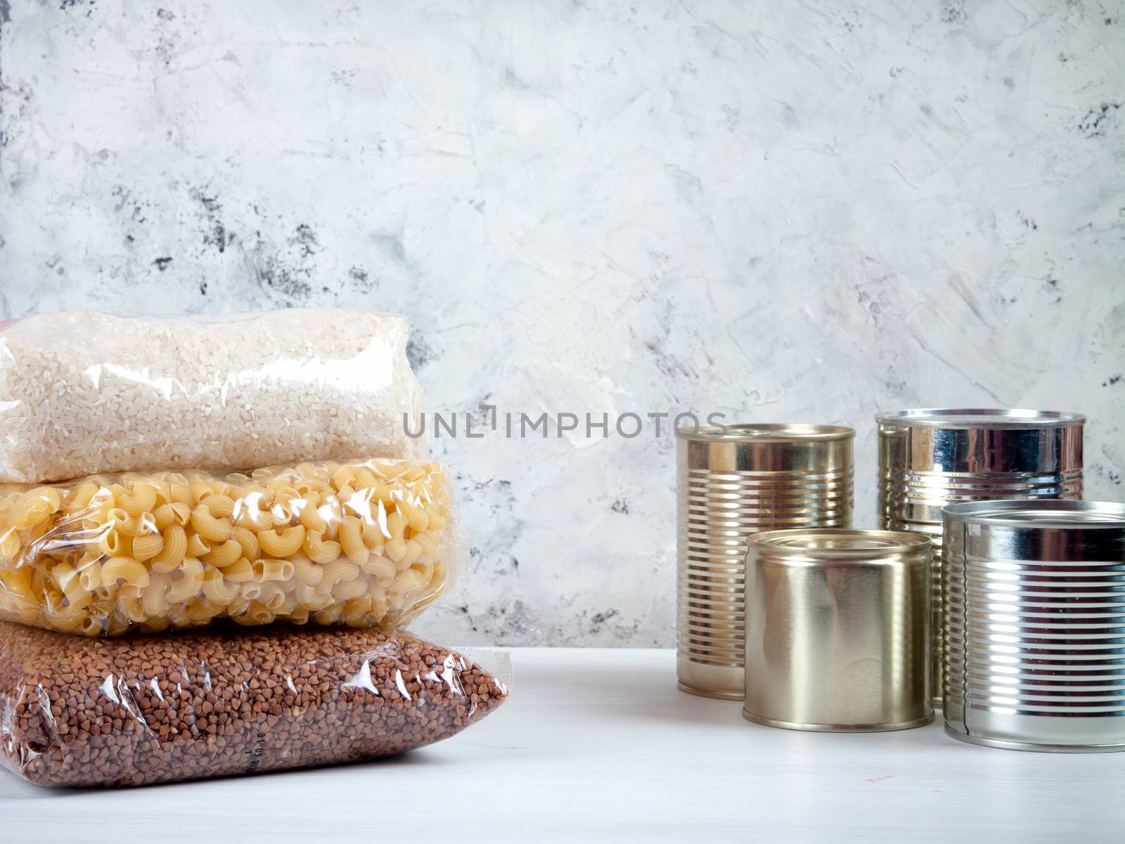 humanitarian assistance for poor and large families. Donation during crisis, pandemic or quarantine. Tin cans, canned food, stew, buckwheat, rice and pasta in transparent bags on white background.