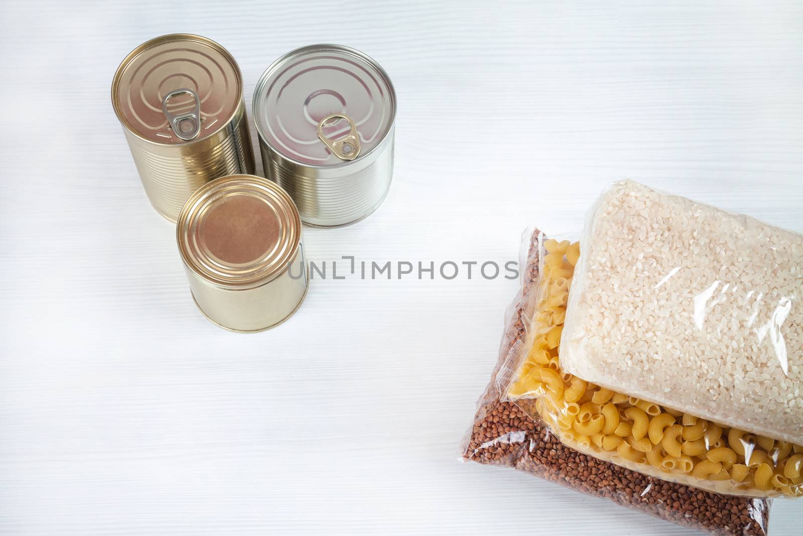 humanitarian assistance for poor and large families. Donation during crisis, pandemic or quarantine. Tin cans, canned food, stew, buckwheat, rice and pasta in transparent bags on white background.