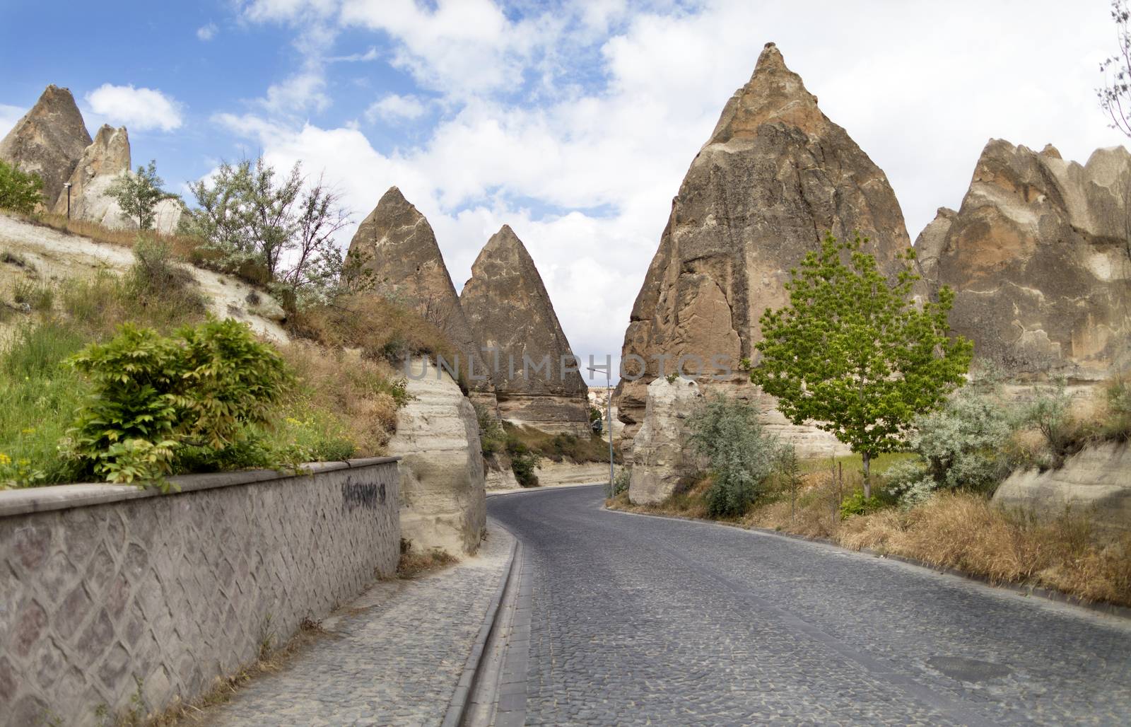 A winding road from paving stones passes near the stone cone houses in the ancient rocks of Goreme, Kappadoki. Rural landscape in the rural way of life of old mountain formations.