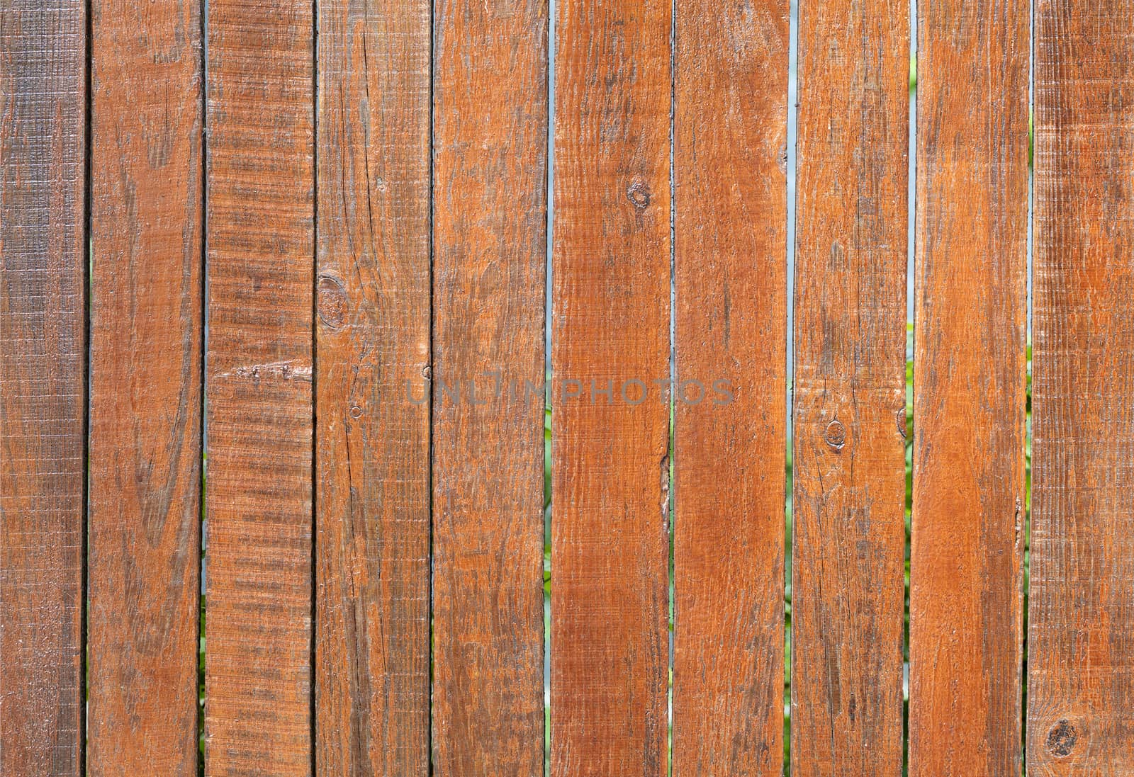 The aged old gray wooden fence is painted with orange paint, close-up