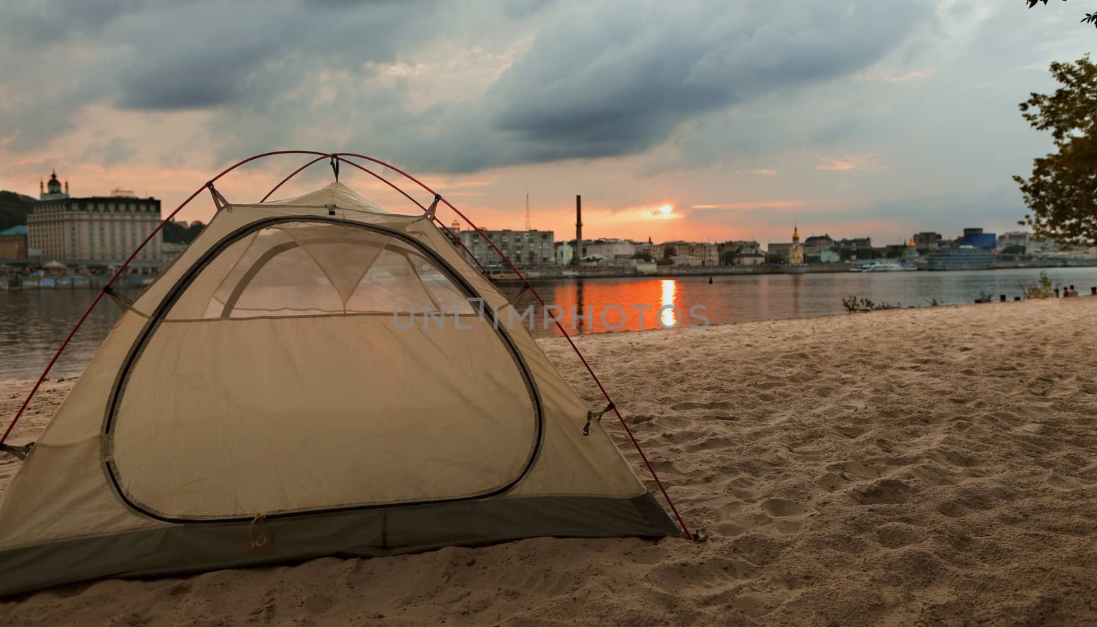 A tent of tourists is located on the city beach of Kyiv with a view of the summer embankment in the rays of the setting sun.