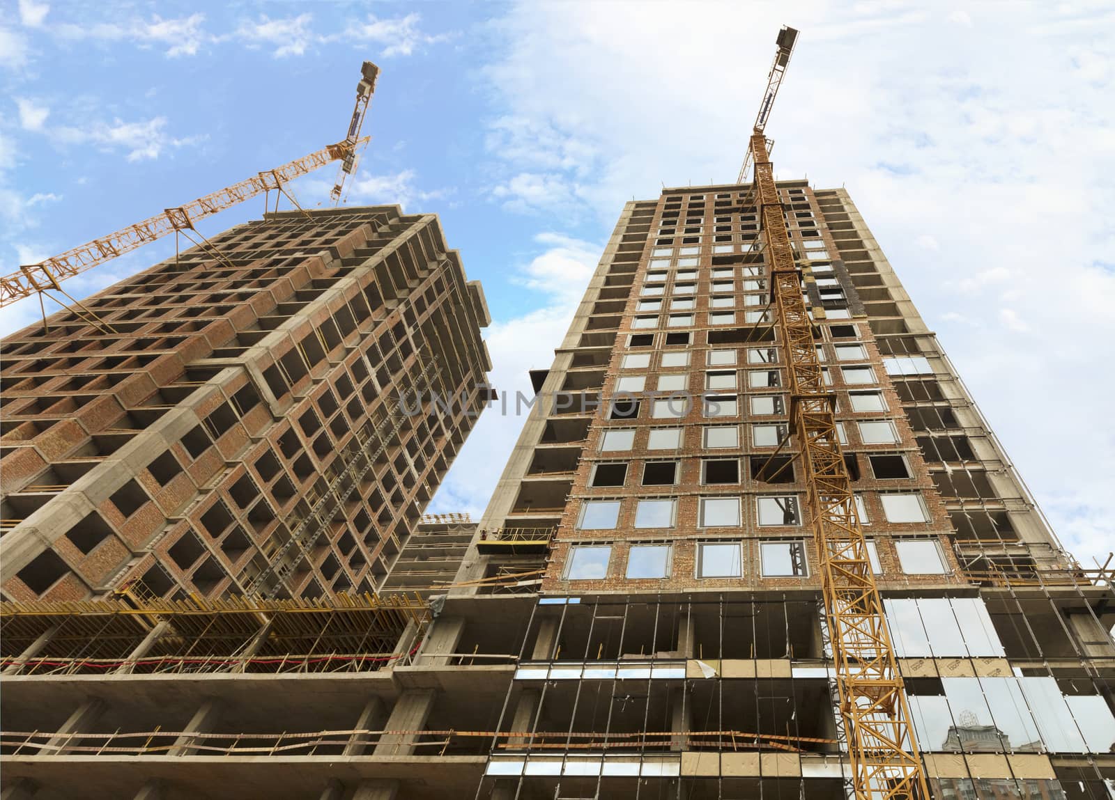 Fragment of facade a house under construction, modern building is under construction, tower building cranes are directed upwards