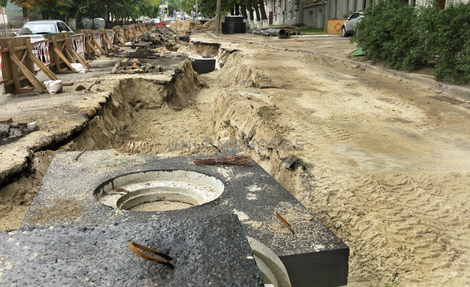 Concrete blocks, wells and pipes of the city collector lie near the excavated trench on the roadway of the street