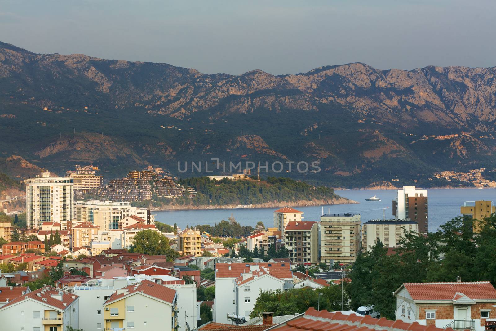 View of the modern city of Budva on the background of a sea bay and a mountain chain in the bright rays of the setting sun