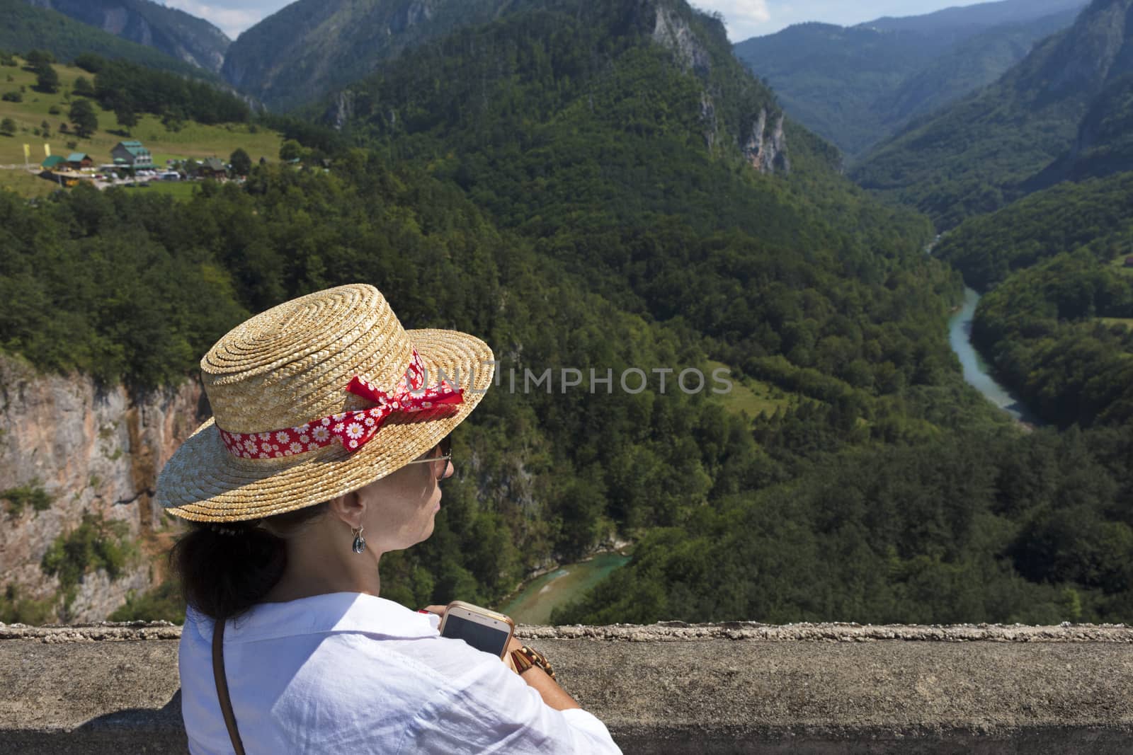 A young woman in a straw hat enjoying the view of a mountain river flowing down the stone gorge by Sergii