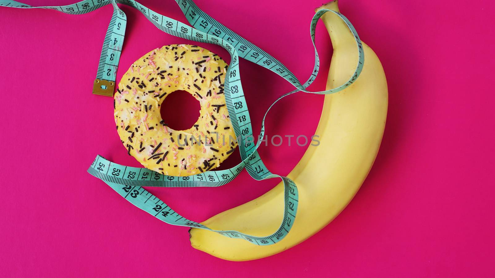 Two types of food, healthy and unhealthy, banana and donut, diet and obesity, health concept on a pink background