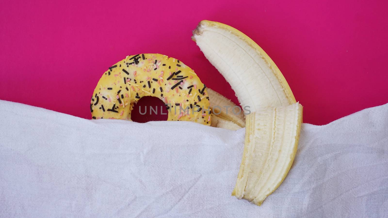 Sweet donut and banana on pink color background. Sex and Erotic concept. Banana hugs donut in bed