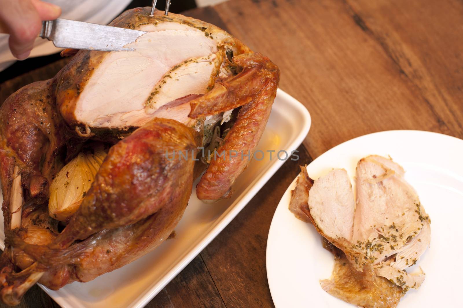 Man carving a delicious browned roast chicken slicing through the white breast meat and serving it onto a plate alongside