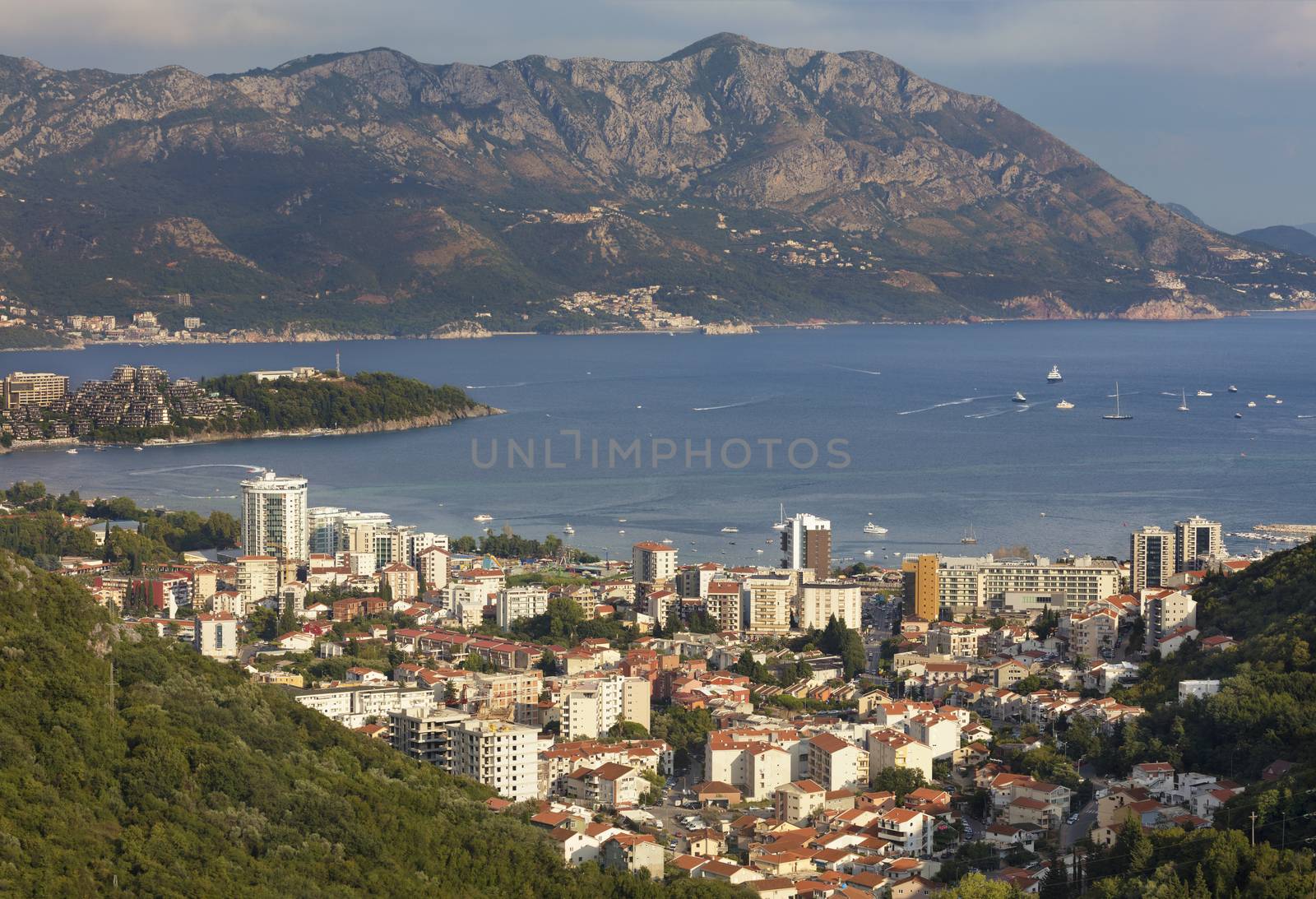 View of the modern city of Budva on the background of a sea bay and a mountain chain in the bright rays of the setting sun