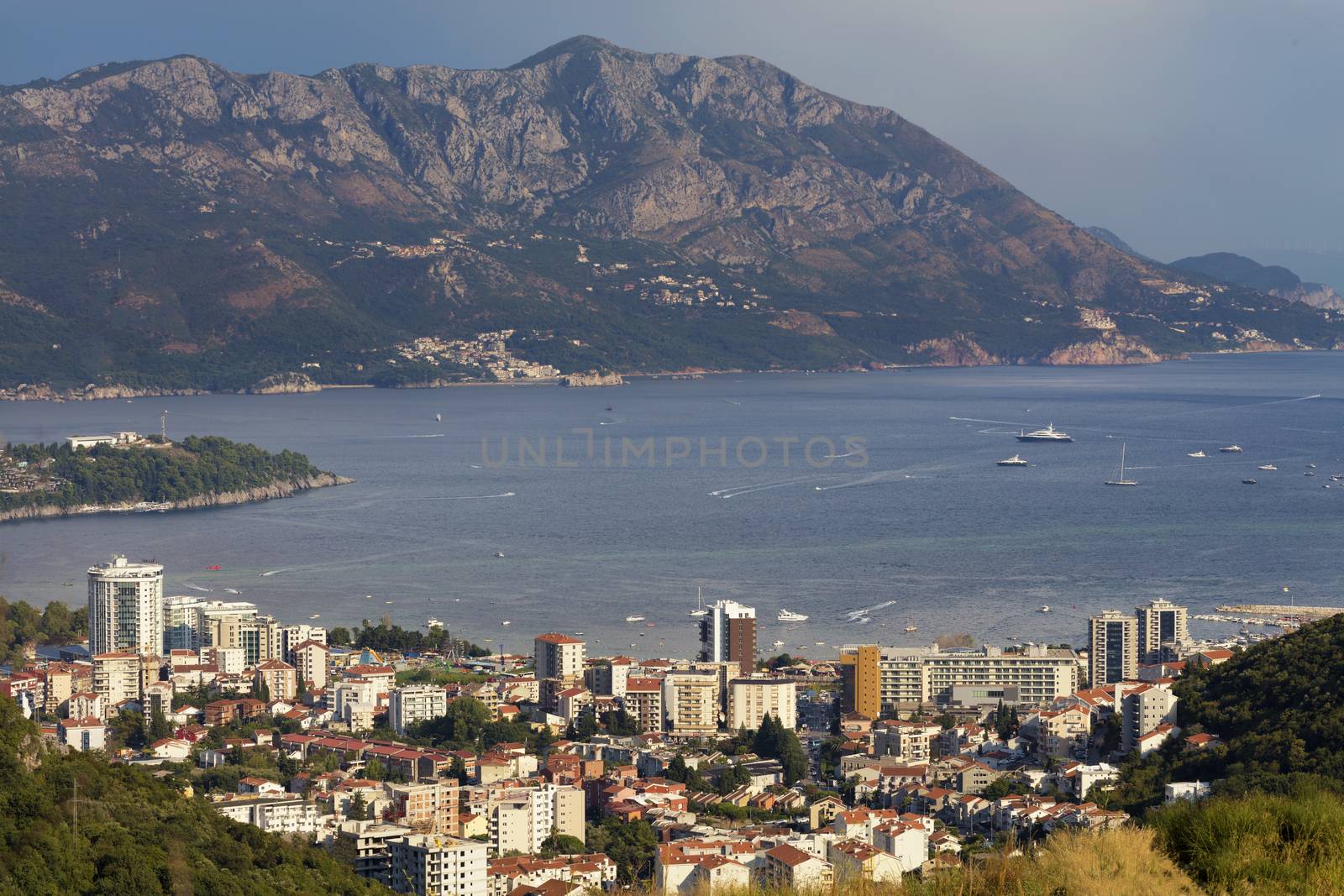 View of the modern city of Budva on the background of a sea bay and a mountain chain in the bright rays of the setting sun