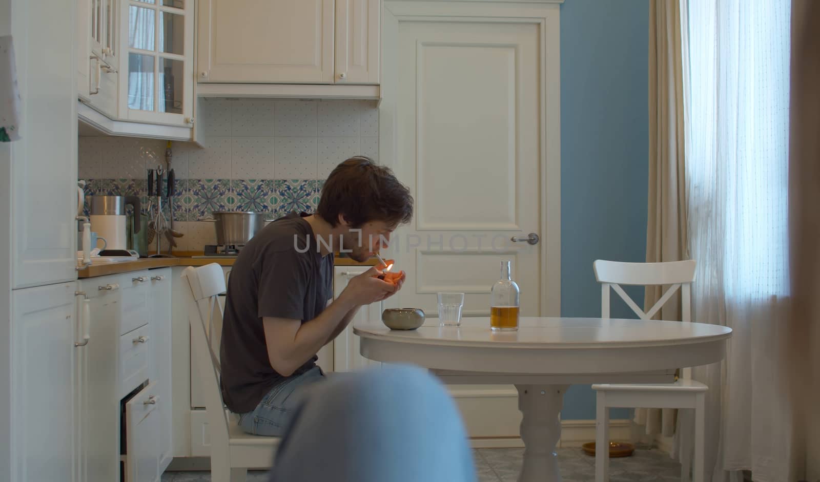 A drunk man lights a cigarette. Man drinking alcohol at home in the kitchen