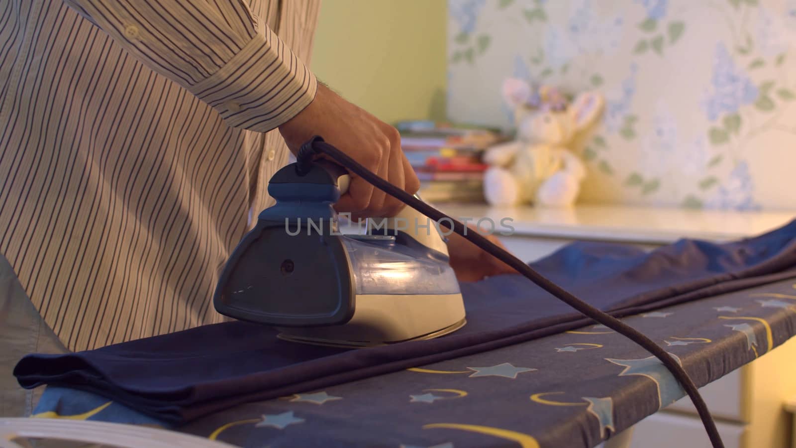 Close up male hand ironing trousers in bright room. Domestic daily life. Household man