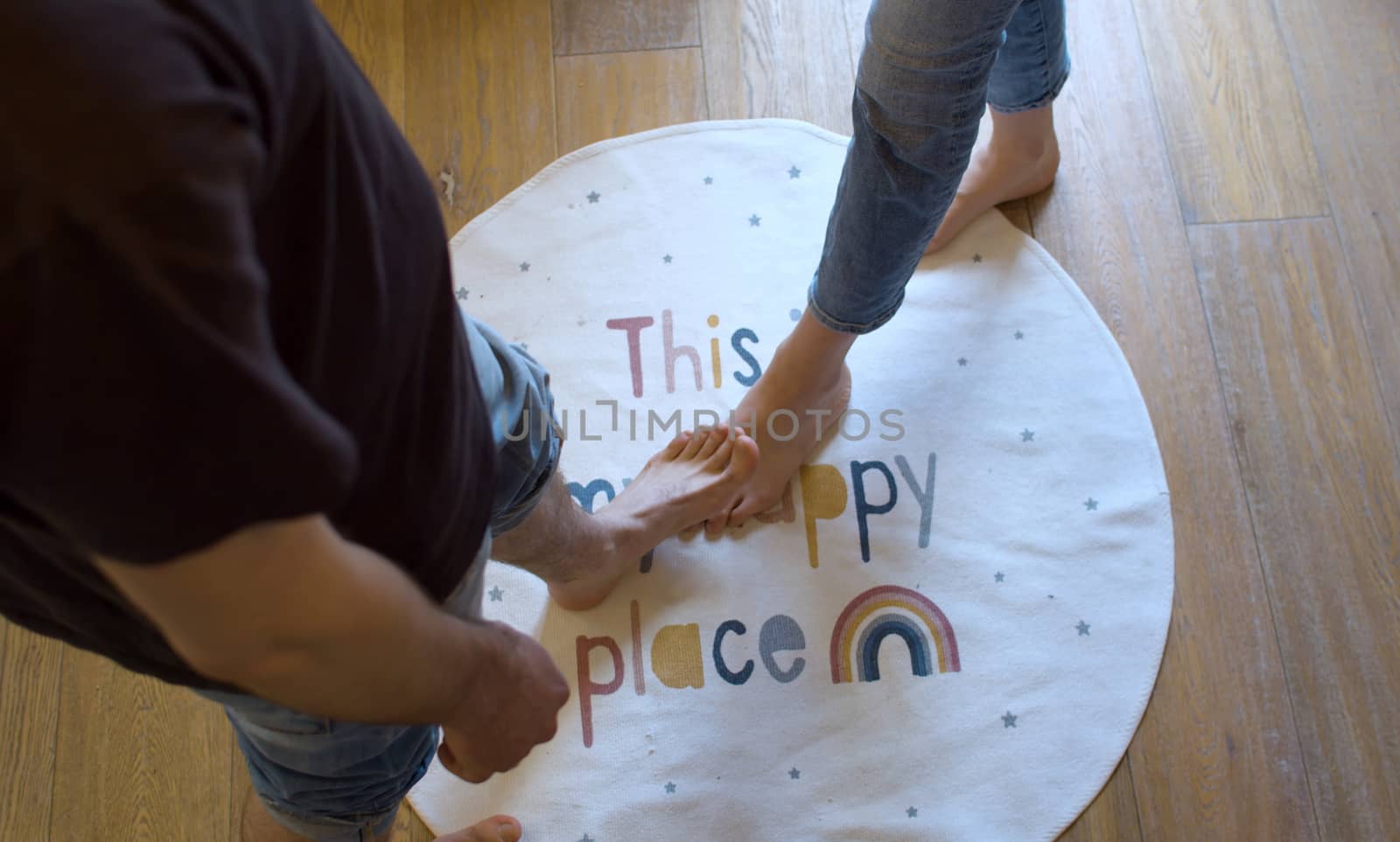 Round rug with the inscription - this is my happy place. Barefoot woman entering a happy place, a barefoot man covering her foot. Symbol of love and trust, top view