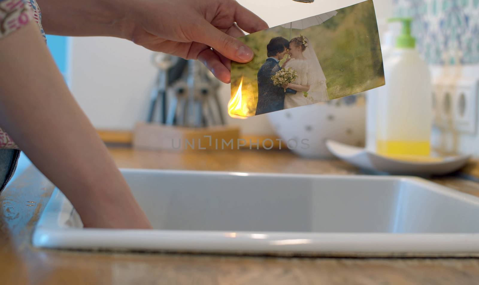 Close up female hands burning a wedding photo in the kitchen sink. Couple quarreled, divorce