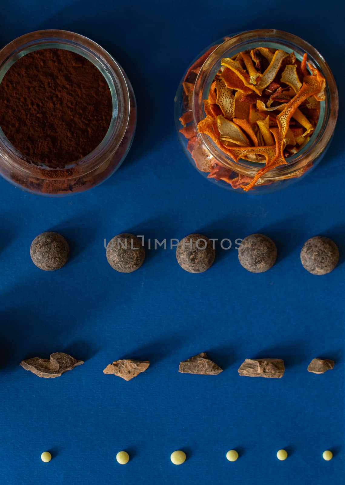 Dark and white chocolate, cocoa and candied orange are laid out on a blue background. Ingredients for making healthy and delicious sugar-free sweets at home. Top view, close-up.