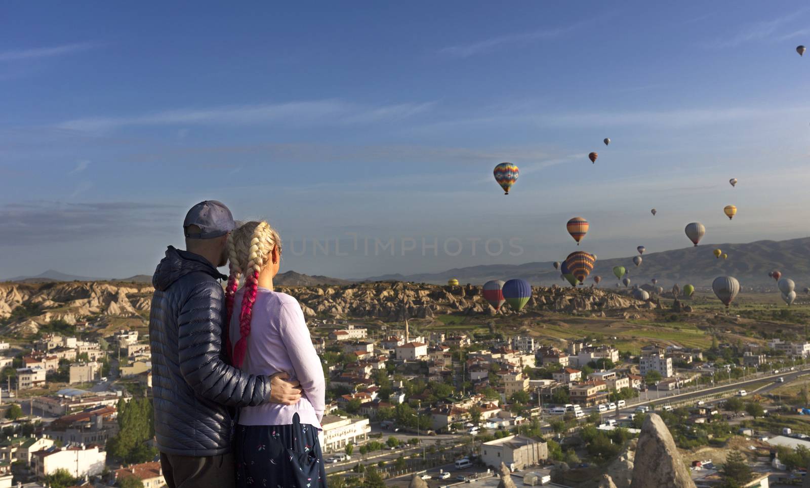 A young couple watches dozens of balloons fly over the valleys in Cappadocia. by Sergii