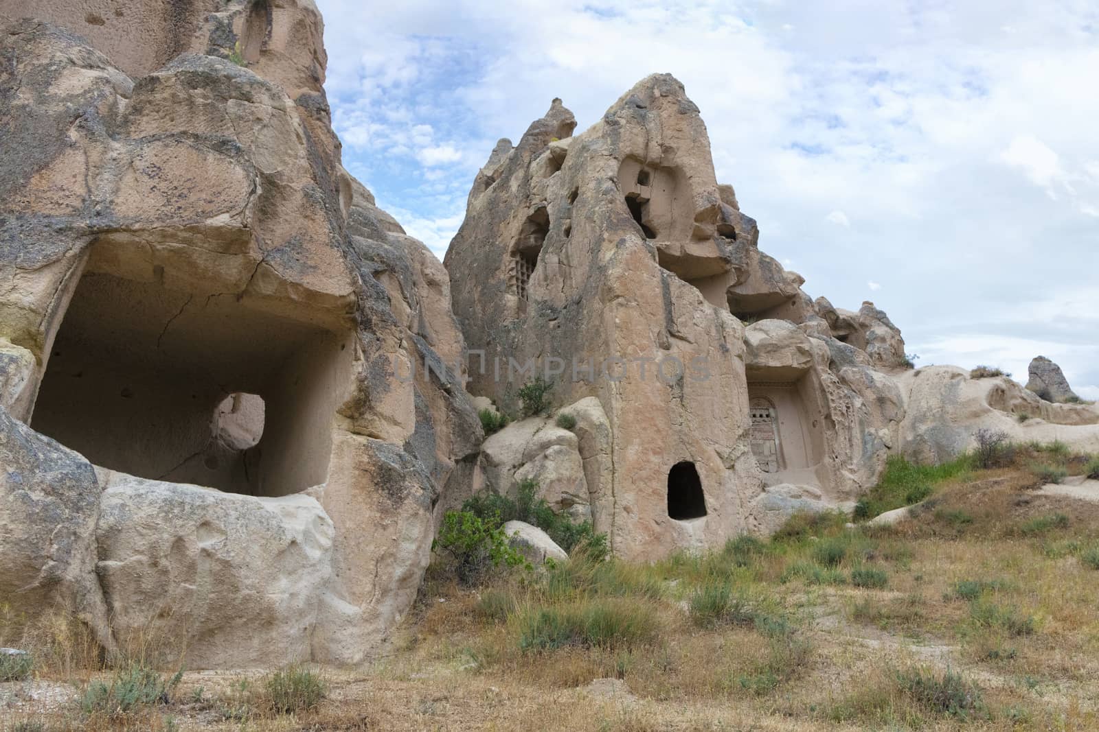 Ancient caves in a mountain landscape in the valleys of Cappadocia against the bright blue and cloudy spring sky of central Turkey