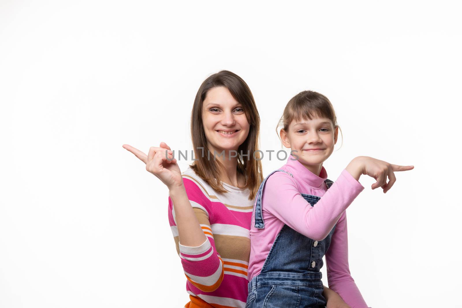 Cheerful mother and daughter point fingers in different directions, isolated on white background